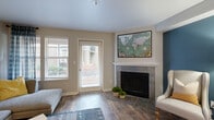 This two-floor residence offers a well-considered layout that balances comfort and functionality throughout. The living room serves as the heart of the home, anchored by a tile-surround fireplace with a classic white mantle. Rich wood-look flooring extends across the space, complemented by a bold teal accent wall that adds a striking focal point. Natural light streams in through a sliding glass door and adjacent window fitted with blinds, creating a bright and welcoming atmosphere.

The dining area transitions seamlessly from the living space, featuring a ceiling fan with integrated lighting and direct sightlines into the kitchen. The kitchen is efficiently designed with white cabinetry, clean white countertops, and stainless steel appliances including a refrigerator, electric range, and over-the-range microwave, all set atop light wood-look flooring.

The bedroom is a calm retreat with plush carpeting, dual windows dressed with elegant curtains that invite natural light, and a sliding closet door with built-in shelving for ample storage. The bathroom features a white vanity with generous counter space, a large mirror, and wood-look flooring, delivering a clean and practical finish. Throughout the space, neutral tones and consistent flooring choices create a cohesive and inviting environment.