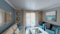 This single-story, one-bedroom, one-bathroom unit offers a cohesive coastal-inspired aesthetic carried throughout every room. The living area serves as the central gathering space, featuring crown molding, hardwood-style flooring, and a sliding glass door fitted with sheer white curtains and vertical blinds that invite abundant natural light while providing access to an outdoor area. Warm neutral walls complement the bright, open feel of the space.

The kitchen is efficiently laid out with white cabinetry, granite-style countertops, subway tile backsplash, and black appliances. It connects seamlessly to a separate dining area, which is defined by a pendant light overhead and provides an intimate setting for meals.

The bedroom is a comfortable retreat, accented with crown molding, a ceiling fan with a light fixture, and stained concrete flooring that adds a distinctive, warm character. The room offers ample wall space and a relaxed, airy ambiance.

The bathroom features a clean, functional design with a full tub-and-shower combination, a dark-finished vanity with a white countertop, and textured neutral walls. Overall, the unit presents a well-organized and stylistically consistent living environment.