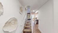 Located in Doral, FL, this two-story, two-bedroom, three-bathroom home offers a thoughtfully designed layout spread across two levels. The main floor features an open-concept living and kitchen area bathed in natural light from large sliding glass doors that frame lush outdoor greenery. The living room is anchored by a ceiling fan and wood-look flooring, creating a warm, inviting atmosphere. The kitchen is outfitted with white shaker cabinetry, a white quartz countertop, a deep single-basin sink, and a full suite of stainless steel appliances including a refrigerator, range, microwave, and dishwasher. Recessed lighting illuminates the space efficiently. A convenient half or full bathroom is also found on this floor. The carpeted staircase with white railings connects both levels, lined with decorative wall accents. Upstairs, the primary bedroom is a spacious and sunlit retreat with ample room, a closet, and an en-suite bathroom. The second bedroom is equally well-appointed with wood-look flooring, a closet, and access to an additional bathroom featuring a tiled shower. Clean white walls throughout both floors lend a bright, neutral backdrop, making this Doral home a well-organized and comfortable residence.
