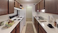 This single-floor, two-bedroom, one-bathroom residence features a thoughtful layout that maximizes functionality across its living spaces. The entry area is finished with tile flooring and provides direct access to the main living areas, with a window that draws in natural light.

The living room offers a comfortable, carpeted space with warm, neutral-toned walls and recessed lighting, creating a welcoming atmosphere. Adjacent to the living room, the dining area accommodates a full dining set beneath a pendant light fixture and includes a window overlooking lush greenery outside.

The galley-style kitchen is efficiently designed with dark wood cabinetry lining both walls, providing ample storage. White appliances, including a range and refrigerator, complement the light countertops, while tile flooring adds durability underfoot.

Both bedrooms are carpeted and feature windows with outdoor views of surrounding trees and landscaping, contributing to a calm, restful ambiance. Each room offers adequate space for standard bedroom furnishings.

The full bathroom includes tile flooring, a vanity with dark wood cabinetry, a mirrored medicine cabinet, and a shower/tub combination, providing all essential amenities in a clean, straightforward layout.