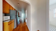 This single-floor residence showcases a blend of classic architectural charm and practical functionality throughout its well-designed layout. Warm hardwood flooring runs continuously through the main living areas and bedrooms, lending a cohesive and inviting feel to the entire space. A distinctive arched doorway serves as a graceful architectural focal point, connecting the living area to the galley-style kitchen corridor and adding character to the overall design.

The kitchen is thoughtfully equipped with stainless steel appliances, including a gas range, refrigerator, and dishwasher, complemented by rich wood cabinetry and granite countertops. An in-unit washer is also conveniently located within the kitchen area. Multiple rooms throughout the residence feature classic cast-iron radiators for heating, as well as wall-unit air conditioners, ensuring year-round comfort. Natural light filters generously through numerous windows fitted with blinds, offering views of the surrounding brick exterior and greenery.

One room features dark speckled flooring and a large double-door closet, providing ample storage. The bathroom retains a timeless aesthetic with its white subway tile surround, soaking tub, and a classic black-and-white basketweave tile floor. The bright, neutral color palette and clean finishes throughout create a comfortable and functional living environment.