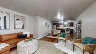 This single-floor residence is designed with an open-concept layout that seamlessly connects the living, dining, and kitchen areas into one cohesive, functional space. The living room offers a comfortable, welcoming atmosphere with warm hardwood-style flooring, neutral gray walls, and ample room for furnishings. The dining area sits adjacent to the kitchen and features a dedicated space for a dining table, accented by decorative wall art that adds a touch of character.

The kitchen is well-equipped with rich dark wood cabinetry, granite-style countertops, and a full suite of stainless steel appliances including a refrigerator, electric range, microwave, and dishwasher. Track lighting overhead enhances the functionality of the cooking space.

The two bedrooms are each carpeted and feature windows that allow natural light to filter in, along with individual climate control units. Each room provides a comfortable and private retreat.

Both bathrooms share a consistent design aesthetic, featuring dark wood vanities with granite-topped single-sink counters, large mirrors, wood-style flooring, and shower-tub combinations. The clean, uniform finishes throughout the unit create a cohesive and modern living environment.