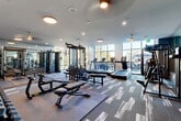 Located at 368 Sublime Summer Lane in Clover, SC, this contemporary fitness center offers a spacious, single-floor layout divided into two distinct workout zones designed to support a full range of exercise modalities. The main strength and cardio area features patterned carpet tile flooring, large floor-to-ceiling windows that flood the space with natural light and offer views of the surrounding greenery. This zone is equipped with a multi-station cable machine, adjustable weight benches, a full dumbbell rack, and multiple treadmills, providing comprehensive options for both resistance training and cardiovascular workouts. Full-length mirrors line portions of the walls, enhancing the sense of openness while allowing users to monitor their form. A second dedicated studio room features smooth hardwood-style flooring and a textured tile accent wall, anchored by a large flat-screen TV for guided workout programming. This area houses cycling bikes, a rowing machine, TRX suspension training benches, and interactive fitness equipment, making it ideal for group or tech-driven training sessions. A glass partition wall connects the two zones while maintaining visual continuity throughout the facility. Recessed and flush-mount ceiling lighting, combined with abundant window light, creates a bright and energizing atmosphere throughout.
