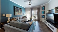 This thoughtfully designed single-floor residence offers a cohesive blend of bold color accents and contemporary finishes throughout its well-organized layout. The living room serves as the heart of the home, featuring a striking teal accent wall, rich hardwood-style flooring, crown molding, and a ceiling fan. Large windows invite abundant natural light, creating a warm and inviting atmosphere. Adjacent to the living area, the dining space is distinguished by a sunny yellow ceiling detail and pendant lighting above a glass-top round table, complemented by hardwood-style floors that flow seamlessly from the main living area. The kitchen is well-equipped with white cabinetry, granite countertops, stainless steel appliances, and hardwood-style flooring, offering both style and functionality. The primary bedroom is a serene retreat with plush carpeting, a ceiling fan, gray accent wall, and an en-suite bathroom reflected through a large dresser mirror. A second bedroom features a rich olive green accent wall, generous natural light from multiple windows, and soft carpeting. The shared bathroom is outfitted with white cabinetry, granite countertops, a shower-tub combination, and hardwood-style flooring. A secondary flexible room with carpeting and neutral tones provides additional versatile living space throughout this well-appointed home.