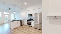 This 1-bedroom, 1-bathroom unit offers a thoughtfully designed layout that maximizes functionality and style. The modern kitchen is a standout feature, equipped with a full suite of stainless steel appliances including a gas range, over-the-range microwave, dishwasher, and refrigerator. White shaker cabinetry extends to the ceiling for ample storage, complemented by a classic subway tile backsplash and dark granite countertops. A peninsula with pendant lighting provides additional prep space and serves as a natural divider between the kitchen and living area. Light wood-tone laminate flooring flows throughout the main living spaces, lending warmth and continuity. The bedroom offers a cozy carpeted floor, natural light from a window with blinds, a ceiling fan, and direct access to a generously sized walk-in closet with multi-tier shelving and hanging rods. The bathroom features large-format tile flooring, a white vanity with dark granite counters, a soaking tub with marble-style tile surround, and built-in shelving. The unit also includes a dedicated laundry area, adding everyday convenience to this clean, modern living space.