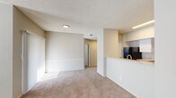 This single-floor residence offers a practical and comfortable layout designed for everyday living. The open living and dining area is finished with plush wall-to-wall carpeting and features a tile-surround fireplace as a central focal point, complemented by large windows fitted with blinds that allow natural light to fill the space. A textured ceiling runs throughout the common areas, adding subtle visual character.

The kitchen is designed with functionality in mind, featuring a raised peninsula counter with granite-style countertops that separates it from the living area. White cabinetry provides ample storage, while black appliances — including a refrigerator and range — offer a clean contrast. A bright overhead panel light illuminates the workspace effectively.

The unit includes multiple bedrooms, each carpeted and finished with neutral-toned walls. The primary bedroom stands out with a ceiling fan, a walk-in closet, and direct access to a private en-suite bathroom. The en-suite is appointed with a granite-style vanity countertop, white cabinetry, and a large mirror. A second full bathroom features wood-look flooring, a single vanity, and a tiled tub-shower combination. An additional bedroom offers a standard closet and a window with outdoor views.