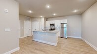 This thoughtfully designed 1-bedroom, 1-bathroom unit offers a cohesive and modern living experience across a single floor. The open-concept kitchen and living area forms the heart of the space, anchored by a central kitchen island with a granite countertop and an integrated sink. White shaker-style cabinetry, a classic subway tile backsplash, and a full suite of stainless steel appliances—including a refrigerator, range, and microwave—complete the kitchen's clean, contemporary aesthetic. Light wood-look flooring extends seamlessly throughout the entire unit, enhancing the bright and airy feel. The living area is spacious and naturally lit, featuring a ceiling fan and access to a private entry door with an adjacent window that brings in outdoor views. The bedroom is a well-sized retreat with a window overlooking greenery, a dedicated closet with built-in shelving, and the same consistent flooring. The bathroom features white cabinetry, granite countertops, and a clean, functional layout that mirrors the refined finishes found throughout the unit. Neutral warm-toned walls and recessed lighting further contribute to the welcoming and cohesive ambiance of this move-in ready space.