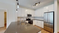 This single-floor residence at 10 Willard Rd in Norwalk, Connecticut, showcases a clean, contemporary design with a cohesive neutral palette and light hardwood flooring that runs throughout the entire space. The open-concept layout connects the kitchen and living area seamlessly, creating a bright and functional environment. The kitchen is a standout feature, equipped with white shaker-style cabinetry extending to the ceiling for ample storage, dark quartz countertops, a subway tile backsplash, and a full suite of stainless steel appliances including a French door refrigerator, electric range, over-the-range microwave, and dishwasher. A central island with an integrated sink and pendant lighting serves as both a prep area and a visual anchor for the space. The living area is generously proportioned, filled with natural light from large windows with outdoor greenery views. Bedrooms are bright and well-sized, each with windows overlooking the surrounding landscape. The bathrooms feature white vanity cabinetry, dark quartz countertops, and large mirrors. Additional storage is provided through a walk-in closet outfitted with wire shelving and organizational fixtures, completing this well-appointed, move-in-ready residence.