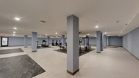 This state-of-the-art fitness center, located at 2800 Washington Ave in Newport News, Virginia, offers a generous 4,060 square feet of space dedicated to health and wellness. The facility features a single-floor layout, maximizing accessibility and flow. The interior is characterized by a modern, minimalist design with light grey walls and contrasting dark grey workout mats strategically placed throughout.

The space is well-equipped with a variety of exercise machines, including treadmills, ellipticals, and strength training equipment. Multiple workout zones cater to different exercise needs, from cardio to weight training. Large, open areas provide ample room for stretching or group activities. The center also includes a mirrored section, ideal for checking form during workouts.

Lighting is a key feature, with recessed ceiling lights ensuring even illumination throughout the space. The combination of light-colored flooring and walls creates a bright, airy atmosphere conducive to an energizing workout experience. Square support columns are seamlessly integrated into the design, providing structural support without impeding movement or sightlines.

Safety features are evident, with visible exit signs and what appears to be a sprinkler system in place. The layout promotes easy navigation and equipment access, enhancing the overall user experience in this comprehensive fitness facility.