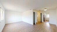This single-floor unit presents a well-organized layout that maximizes functionality across its living spaces. The main living area is bright and open, finished with light-toned wood flooring that extends throughout much of the unit, complemented by crisp white walls that enhance the sense of space and airiness. Louvered closet doors and ceiling-mounted vents add practical, built-in storage and climate control features.

The kitchen is designed for efficiency, featuring a galley-style configuration with rich dark wood cabinetry, granite-look countertops, a stainless steel double sink, and full-size appliances including a refrigerator and range. A window above the exterior door allows natural light to brighten the workspace.

The bedroom is a comfortable, well-proportioned room finished with plush neutral carpeting underfoot and a window fitted with white horizontal blinds that provide both privacy and natural light. A ceiling-mounted light fixture completes the room.

The bathroom is clean and functional, outfitted with a white vanity, a combined tub and shower unit with grab bar accessibility, and wood-look flooring that ties cohesively to the rest of the unit. Overall, the space offers a straightforward and practical living environment with consistent, neutral finishes throughout.