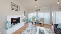 This two-floor home impresses with its dramatic vaulted ceilings and an abundance of natural light throughout. The main living area is a standout space, featuring soaring ceilings with striking height, warm hardwood flooring, and a wall of floor-to-ceiling sliding glass doors dressed with vertical blinds that flood the room with daylight. A classic fireplace with a clean white surround serves as a focal point, complemented by pendant lighting that adds a modern touch to the open layout. The living area also accommodates a sizable entertainment setup, with towering windows that amplify the sense of volume and openness.

The kitchen is functional and well-appointed, featuring black appliances including a full-size refrigerator and range, white upper cabinetry, and hardwood flooring consistent with the rest of the main level.

One of the home's most notable features is a dedicated billiard room, complete with a full-size pool table, wall-mounted television, ceiling fan, and bar-height seating — an ideal space for recreation and entertaining. The room benefits from its own windows, providing natural light and a relaxed atmosphere.

A staircase connects the two floors, and the overall layout, as seen in the aerial model view, reveals a spacious and thoughtfully arranged floor plan designed for both comfort and functionality.