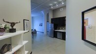 This single-floor loft showcases a striking industrial aesthetic, blending raw architectural details with contemporary finishes to create a stylish and functional living space. The open-concept layout allows the kitchen, dining, and living areas to flow seamlessly into one another, fostering a sense of spaciousness and connectivity throughout.

The kitchen is outfitted with dark, espresso-toned cabinetry that contrasts cleanly against light countertops, and is equipped with stainless steel appliances including a full-size refrigerator and dishwasher. A functional sink completes the workspace, making the kitchen as practical as it is visually appealing.

Underfoot, polished concrete floors run throughout the space, reinforcing the industrial character while remaining easy to maintain. Overhead, exposed ceiling infrastructure — including ductwork and a grid of track lighting — adds depth and an urban warehouse sensibility. Structural columns punctuate the open floor plan, serving as architectural accents that define zones within the space without interrupting the open feel.

The living area is bathed in a cool ambient light, with framed artwork adorning the walls, adding a cultivated, gallery-like quality. The overall ambiance is modern and urban, appealing to those who appreciate clean lines, open layouts, and industrial-chic design elements.