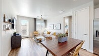 This single-floor, 2-bedroom, 2-bathroom residence offers a thoughtfully designed open-concept layout that maximizes functionality and comfort. The combined kitchen and living area serves as the heart of the home, where warm wood-look flooring flows seamlessly throughout. The kitchen is equipped with stainless steel appliances, including a French door refrigerator, range, microwave, and dishwasher, all complemented by crisp white cabinetry, quartz countertops, and a peninsula island with bar seating — ideal for casual dining or entertaining. The adjacent living area is bright and airy, benefiting from large windows with ample natural light and direct access to an outdoor patio. The primary bedroom features a distinctive two-tone accent wall in muted blue and white tones, wood-look flooring, and a well-organized walk-in closet with multi-tier shelving and hanging rods. The second bedroom is equally comfortable with access to its own closet. The bathrooms include clean, modern finishes, with one featuring an in-unit stacked washer and dryer. A hallway with a sleek frosted glass sliding door connects the private quarters. The overall aesthetic is clean, modern, and welcoming throughout.