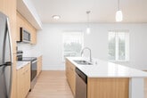 This well-appointed single-floor unit offers a clean, contemporary design with a cohesive neutral palette and light wood flooring that flows throughout the main living areas. The open-concept kitchen is a standout feature, equipped with warm wood-toned flat-front cabinetry, a white subway tile backsplash, white quartz countertops, stainless steel appliances including a refrigerator, range, and built-in microwave, and a large central island with pendant lighting and an integrated sink. The adjoining living and dining area is generously proportioned, bathed in natural light from multiple windows fitted with horizontal blinds that frame views of the surrounding neighborhood and greenery. The hallway connects to multiple bedrooms, each featuring soft carpet flooring, natural light from large windows, and access to closet storage. A dedicated room with hardwood-style flooring offers additional flexible use. Two full bathrooms serve the unit — one featuring a combined tub and shower with chrome fixtures and a wood-accented vanity, and another with a spacious vanity, large mirror, and separate shower. Throughout, the unit maintains a bright, clean aesthetic suited to modern living.