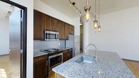 Situated at 272 S Front St in Columbus, Ohio, this single-floor space showcases a compelling mix of industrial loft aesthetics and contemporary design. Soaring ceilings and large, grid-paned windows flood the interior with natural light, creating an open and airy atmosphere that highlights the thoughtful use of space throughout.

The kitchen is a standout feature, boasting rich dark-stained cabinetry, a classic subway tile backsplash, and gleaming granite countertops. A central island with an undermount stainless steel sink and a gooseneck faucet serves as both a functional workspace and a gathering point. Stainless steel appliances, including a refrigerator, range, and built-in microwave, complete the well-appointed cooking area. Overhead, a curated mix of Edison bulb pendant lights and industrial-style cage fixtures add warm, ambient illumination that complements the space's urban character.

The warm-toned hardwood flooring extends through the main living areas, grounding the space and adding a natural contrast to the exposed mechanical elements visible at the ceiling. The overall ambiance is sophisticated yet approachable, reflecting the vibrant energy of Columbus's downtown Front Street corridor.