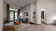 This thoughtfully designed single-floor residence blends modern aesthetics with functional living. The open-concept living area immediately draws attention with its soaring ceilings, light wood-style flooring, and a striking accent wall finished in a textured blue-grey wallcovering. A ceiling fan with a contemporary pendant-style fixture adds visual interest overhead, while large windows and glass doors allow abundant natural light and views of lush greenery outside. Built-in corner shelving and a substantial built-in bookcase unit provide ample display and storage space throughout the living area.

The kitchen is well-appointed with grey shaker-style cabinetry, a subway tile backsplash, white countertops, stainless steel appliances, and under-cabinet lighting. A seamlessly integrated built-in desk workstation sits adjacent to the kitchen, offering a dedicated workspace with overhead open shelving.

Both bedrooms feature plush carpeting, ceiling fans, and large windows that invite natural light. The primary bedroom includes a spacious walk-in closet with multi-level hanging and shelving systems.

The two bathrooms are finished with marble-style floor and wall tile, soaking tubs with shower combinations, grey cabinetry, and white quartz countertops, delivering a clean, contemporary aesthetic throughout.