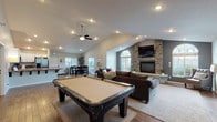Located at 12423 East Mansfield Avenue in Spokane Valley, WA, this single-floor community clubhouse offers a well-appointed gathering space designed for both recreation and relaxation. The centerpiece of the facility is a generous great room with soaring vaulted ceilings, rich hardwood flooring, and a dramatic floor-to-ceiling stacked stone fireplace flanked by arched windows that fill the space with natural light. A full-size pool table anchors the game area, while a comfortable seating arrangement with plush sofas creates an inviting lounge atmosphere. Adjacent to the great room, a bright dining area features a large bar-height table and ample windows overlooking the surrounding landscape. The fully equipped kitchen boasts rich granite countertops, crisp white cabinetry, stainless steel appliances including a gas range, microwave, and refrigerator, and an open pass-through bar that connects seamlessly to the main gathering area. A dedicated fitness center provides a comprehensive workout experience, outfitted with cardio machines including treadmills and ellipticals, a multi-station cable machine, free weights, and large windows that bring in natural light. A separate lounge area with hardwood and carpeted flooring offers additional seating for smaller gatherings. Throughout, recessed lighting and ceiling fans contribute to a comfortable, functional ambiance.