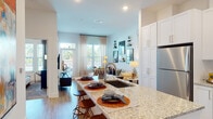Located at 2620 Mall of Georgia Blvd in Buford, Georgia, this well-appointed single-floor residence offers a thoughtfully designed open-concept layout that seamlessly connects the kitchen, dining, and living areas. The kitchen is a standout feature, boasting crisp white shaker cabinetry extending to the ceiling, granite countertops, a large center island with a deep undermount sink and bar seating, and a full suite of stainless steel appliances including a refrigerator, range, microwave, and dishwasher. Light wood-style flooring flows throughout the main living areas, complementing the bright, neutral color palette. The living room is bathed in natural light from large windows and sliding glass doors that open to a private balcony, creating an inviting and airy ambiance. The bedroom features plush carpeting, generous windows with outdoor views, and ample natural light. The bathroom offers a granite-topped vanity with white cabinetry and wood-style flooring. A dedicated laundry area accommodates a stacked washer and dryer unit alongside open shelving and closet rod storage. Recessed lighting throughout enhances the clean, modern aesthetic of this well-designed residence.