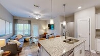 Located in Chester, Virginia, this single-floor, two-bedroom, two-bathroom home offers a thoughtfully designed open-concept layout. The kitchen serves as a central hub, featuring granite countertops, white shaker cabinetry, stainless steel appliances including a range, over-the-range microwave, and refrigerator, and a large island with a double-basin sink and pendant lighting overhead. The kitchen flows seamlessly into the living room, which is highlighted by wood-style flooring, a ceiling fan, and large windows and a glass door that invite natural light and provide outdoor views. The neutral wall tones throughout create a cohesive, calming ambiance.

The primary bedroom offers comfortable proportions, carpet flooring, a ceiling fan, and a window with outdoor views. The second bedroom is similarly appointed with carpet and a ceiling fan. Both bathrooms include granite-topped vanities, white cabinetry, and wood-style tile flooring. A dedicated in-unit laundry area houses a full-size top-load washer and dryer with overhead shelving. Two closets provide additional storage. The entrance offers a welcoming transition into the home's clean, modern interior.