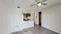This single-floor unit is thoughtfully designed with a clean, contemporary aesthetic throughout. The open-concept living and dining area is anchored by warm hardwood-style flooring in a light gray tone and a ceiling fan with integrated lighting. Large sliding glass doors lead to a private balcony, flooding the space with natural light and providing outdoor views. The living area flows seamlessly into the kitchen, which is separated by a peninsula counter featuring a light stone-look surface — ideal for casual dining or food preparation. The kitchen is well-appointed with dark espresso cabinetry extending to the ceiling, a classic white subway tile backsplash, stainless steel appliances including a side-by-side refrigerator with ice and water dispenser, an electric range, and an over-the-range microwave. Track lighting overhead provides focused task illumination. The bedroom is generously proportioned with dark hardwood-style flooring, neutral gray walls, and direct access to a walk-in closet with built-in shelving. The en-suite bathroom features a full-size soaking tub with a curved shower rod, tile surround, and a vanity with dark wood cabinetry and a mirror. A utility panel is conveniently located near the main entry.