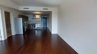 This single-floor space showcases a thoughtfully designed open-concept layout that seamlessly connects the living area and kitchen, creating a spacious and functional environment. Rich, dark hardwood floors run throughout, adding warmth and elegance to the clean, modern aesthetic.

The kitchen is a standout feature, equipped with stainless steel appliances including a gas range, wall oven, microwave, and a full-size refrigerator. A sleek stainless steel range hood hangs above the cooktop, serving as both a practical and stylish element. Dark cabinetry with a contemporary finish provides ample storage, while the kitchen's open orientation toward the living area makes it ideal for entertaining.

Crisp white walls and ceilings enhance the sense of openness, while recessed and pendant lighting illuminate the space with a warm glow. The entry door is positioned at the rear of the kitchen corridor, providing a defined sense of arrival. The expansive open floor plan of the living area offers generous flexibility for furniture arrangement and daily living. Overall, the space presents a polished, modern interior with high-quality finishes and a cohesive design sensibility throughout.