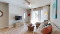 This 2-bedroom, 2-bathroom single-floor residence delivers a well-appointed living experience with a functional and inviting layout. The living room serves as the heart of the home, featuring warm wood-look flooring that extends throughout the space, creating a cohesive and modern aesthetic. A ceiling fan with a light fixture adds both comfort and practicality, while large sliding glass doors flood the room with abundant natural light and provide direct access to the outdoors, offering views of lush landscaping. Neutral-toned walls provide a versatile backdrop that complements a variety of design styles. The living area offers ample room for comfortable seating and entertainment, making it ideal for both relaxing and hosting guests. The two bedrooms provide private retreats, each accompanied by its own full bathroom, offering convenience and privacy for residents or guests. The overall ambiance of the home is bright, airy, and welcoming, with a clean design that balances style and functionality. The combination of natural light, quality flooring, and an efficient floor plan makes this residence an attractive and comfortable place to call home.