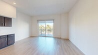 Located at 1640 East Plaza Boulevard in National City, CA, this well-designed one-bedroom, two-bathroom residence offers a clean, modern aesthetic across a single floor. Light-toned hardwood-style flooring runs throughout, complementing the crisp white walls and creating a bright, cohesive feel.

The open-concept living, dining, and kitchen area serves as the heart of the home. The kitchen is outfitted with rich dark-wood cabinetry, stainless steel appliances including a refrigerator, dishwasher, range, and microwave, plus ample counter space. Recessed lighting and soaring ceilings add to the airy atmosphere of this shared space.

The bedroom is a comfortable, sun-filled retreat featuring a large closet with louvered doors and a window with views of surrounding greenery. A private balcony accessible via sliding glass doors with a roller shade offers pleasant outdoor views of mature palm trees, extending the living space outdoors.

A hallway connects the main living areas to the bedroom and two bathrooms. One bathroom doubles as a laundry room for added convenience. The full bathroom features a clean, contemporary design with a dark-wood vanity, white undermount sink, large mirror, and a tub/shower combination with chrome fixtures. The overall ambiance is modern, minimal, and move-in ready.