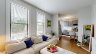 Located on Laurel Avenue West in Minneapolis' desirable Lowry Hill neighborhood, this thoughtfully designed one-bedroom, one-bathroom unit makes excellent use of its compact footprint across a single floor. The open-concept living and kitchen area anchors the space, with large windows fitted with horizontal blinds flooding both zones with natural light and offering views of the surrounding neighborhood streetscape. Warm hardwood flooring runs throughout the main living areas, lending continuity and a polished feel. The living room accommodates a generous sectional sofa and features a wall-mounted TV, creating a comfortable and functional gathering space. The kitchen is outfitted with grey shaker-style cabinetry, stainless steel appliances including a refrigerator, range, and microwave, white subway tile backsplash, and light countertops. A butcher-block dining table with seating sits at the kitchen's edge, ideal for casual meals. The bedroom features carpeted floors, a large window with neighborhood views, wall sconces, and a clean, restful ambiance. The bathroom includes a subway-tiled walk-in shower with a mosaic tile floor. A dedicated in-unit laundry closet with a stacked washer and dryer adds everyday convenience, completing this well-appointed Minneapolis residence.