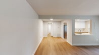 This 680-square-foot, one-bedroom, one-bathroom apartment at 8800 Queensmere Place in Richmond, Virginia offers a clean, modern aesthetic throughout its single-floor layout. Light hardwood flooring runs continuously across all rooms, creating a cohesive and airy feel.

The combined kitchen and living area forms the heart of the unit. The galley-style kitchen is outfitted with two-tone cabinetry — warm wood lower cabinets paired with crisp white upper cabinets — complemented by white quartz countertops and stainless steel appliances, including a refrigerator, range, microwave, and dishwasher. A pass-through window connects the kitchen to the living area, enhancing the open-concept feel. The living room benefits from a striking wall of French doors that flood the space with natural light and provide outdoor views.

The 200-square-foot primary bedroom features a window with exterior views, a built-in closet with shelving and hanging rods, and neutral grey-toned walls. The full bathroom includes a tiled tub-shower combination, toilet, and a framed vanity mirror. A connecting hallway ties all rooms together efficiently. The unit's neutral color palette and contemporary finishes make it a versatile and inviting living space.