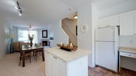 This well-designed three-story residence offers a thoughtfully arranged layout across multiple levels, connected by a central staircase. The main living area is anchored by a tile-surround fireplace and flows seamlessly into a carpeted dining space, creating a warm and cohesive gathering area. A ceiling fan overhead and a sliding glass door leading to a private balcony bring in natural light and outdoor views, enhancing the open feel of the living room.

The kitchen features white cabinetry, light countertops, hardwood-style flooring, and a central island that provides additional workspace and casual dining potential. White appliances, including a refrigerator, dishwasher, stove, and microwave, are neatly integrated, while a large window above the sink offers pleasant outdoor views and natural light.

The bedrooms are carpeted and generously sized, each featuring large windows that frame tree-lined views and multiple closets for ample storage. One bedroom includes a walk-in closet configuration, offering practical organization. The bathrooms are clean and functional, with one featuring a glass-door stand-up shower and another equipped with a tub-shower combination, a single vanity with mirrored medicine cabinet, and tile flooring.