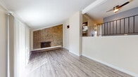 This thoughtfully designed home offers a blend of classic character and modern updates across a well-utilized floor plan. The main living area makes an immediate impression with its full-wall brick fireplace, serving as a striking focal point beneath vaulted ceilings. Light gray hardwood-style flooring flows through the living and entry areas, complementing the neutral wall tones and creating a clean, cohesive aesthetic. An open-railing staircase with sleek black metal balusters adds architectural interest while maintaining an open, airy feel between levels. Large sliding glass doors and windows fitted with vertical blinds invite abundant natural light throughout. The kitchen features rich dark wood cabinetry paired with granite countertops and a double stainless steel sink, offering both style and functionality. A convenient in-unit laundry closet houses a stacked Whirlpool washer and dryer. The bathrooms are finished with granite-topped dark wood vanities and framed mirrors. Bedrooms are carpeted for comfort, with multiple rooms offering walk-in or organized closet storage and outdoor access via sliding doors with views of the surrounding exterior. The overall ambiance is bright, clean, and move-in ready.