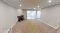This two-story space offers a thoughtfully designed layout with clean, neutral finishes throughout. The living area serves as a central gathering space, finished with plush wall-to-wall carpeting in a warm beige tone that adds comfort underfoot. A sleek, tile-surround corner fireplace anchors one end of the room, providing both a functional heating element and a stylish focal point. Recessed lighting is evenly distributed across the ceiling, offering consistent, adjustable illumination, while crown molding along the ceiling perimeter adds a refined architectural detail.

Natural light flows generously into the living area through a large sliding glass door fitted with vertical blinds, offering both privacy control and access to an outdoor area. The neutral wall tones complement the overall palette, creating a bright and airy atmosphere. The open feel of the main living space is enhanced by its generous proportions, making it versatile for various furniture arrangements. The two-floor layout provides separation between living and private areas, contributing to a functional and well-organized flow throughout the home.