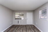 Located at 1005 Elberta Rd in Warner Robins, Georgia, this single-story home offers a straightforward and functional layout finished with consistent wood-look vinyl plank flooring throughout. The neutral gray walls and white trim create a clean, cohesive aesthetic across all rooms.

The kitchen is outfitted with white cabinetry extending to the upper walls for ample storage, gray laminate countertops, a double-basin sink, and a white electric range with overhead ventilation. A wall-mounted air conditioning unit and a window with blinds provide both climate control and natural light. A pass-through opening connects the kitchen to the adjacent living area, enhancing the sense of openness between the spaces.

The living area is bright and open, benefiting from multiple windows that allow natural light to fill the room. A wall-mounted heating unit is conveniently positioned near the entry. The entry door is flanked by two windows, offering views of the surrounding greenery.

The bedrooms are well-proportioned, each featuring wood-look flooring, neutral walls, and ceiling light fixtures. One bedroom includes access to additional rooms, indicating a connected interior layout with closet and hallway access.

The bathroom is finished with white subway tile wainscoting, a bathtub and shower combination, a window for natural ventilation, and wood-look flooring that ties the space together with the rest of the home.