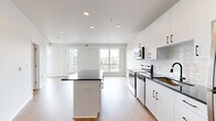 Located at 1636–1648 NW 38th St in Kansas City, MO, this thoughtfully designed single-floor residence combines contemporary finishes with a bright, open layout. The kitchen serves as a central highlight, showcasing crisp white cabinetry with matte black hardware, dark granite countertops, a center island with additional counter space, and a full suite of stainless steel appliances including a range, microwave, and refrigerator. A white subway tile backsplash adds a clean, modern touch. Warm hardwood-style flooring flows seamlessly throughout the entire unit, creating a cohesive and inviting atmosphere. The living area is generously proportioned, featuring a curved wall of large windows that flood the space with natural light and offer views of the surrounding neighborhood. The open entry area connects the kitchen and living spaces in a practical, free-flowing arrangement. The bathroom is finished to a high standard, featuring a walk-in glass-enclosed shower with large-format white tile, a dark granite vanity top, white cabinetry, and matching black hardware. A spacious walk-in closet provides substantial storage with built-in wire shelving and hanging rods. Recessed lighting throughout the unit ensures consistent illumination, complementing the clean, neutral color palette that defines the overall aesthetic of this well-appointed residence.