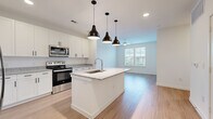 This thoughtfully designed one-bedroom, one-bathroom residence in Austin, TX offers a clean, modern aesthetic throughout its well-appointed single floor. The open-concept kitchen and living area serves as the heart of the home, anchored by a large central island with granite countertops, an undermount sink, and a dishwasher. A trio of matte black pendant lights adds a contemporary touch above the island. The kitchen is further equipped with stainless steel appliances — including a French door refrigerator, electric range, and built-in microwave — alongside crisp white shaker-style cabinetry and recessed lighting. Light wood-look flooring flows seamlessly through the main living area, where a ceiling fan and large windows allow for natural light and outdoor views. The bedroom features plush carpet, a ceiling fan, and dual windows overlooking the surrounding landscape, creating a comfortable retreat. A dedicated walk-in closet with built-in shelving provides ample storage. The full bathroom is finished with granite countertops, white shaker cabinetry, a deep soaking tub with subway tile surround, and a spacious walk-in closet accessible directly from the bath. Light wood-look flooring carries through this space, tying the home together cohesively.