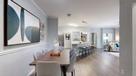 This single-story residence offers a thoughtfully designed layout across three bedrooms and two bathrooms. The open-concept living, dining, and kitchen area serves as the heart of the home, featuring wood-style flooring throughout and a neutral gray-toned color palette that creates a cohesive, modern aesthetic. The living room receives ample natural light through large windows dressed with light curtains, while a built-in niche in the hallway adds a subtle architectural detail.

The kitchen is well-equipped with stainless steel appliances, white shaker-style cabinetry, a gray subway tile backsplash, and a generous island with a white quartz countertop that accommodates bar seating beneath pendant lighting. The adjoining dining area features wainscoting along the lower walls and crown molding details.

The primary bedroom is a comfortable retreat with vaulted ceilings, a ceiling fan, accent wall, and wood-style flooring. Additional bedrooms share similar design elements. Both bathrooms include a tub-shower combination, white vanity cabinetry, tile flooring, and framed mirrors. A dedicated laundry room with overhead shelving and an outdoor patio round out the functional amenities of this residence.