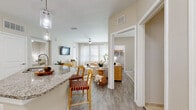 Located at 6608 S West Shore Blvd in Tampa, Florida, this well-appointed single-floor residence offers a thoughtfully designed open-concept layout with contemporary finishes throughout. The kitchen serves as a central highlight, featuring crisp white shaker cabinetry, a subway tile backsplash, stainless steel appliances, and a generously sized granite-topped island with an integrated sink and bar seating — ideal for both meal preparation and casual dining. Pendant lighting adds a refined touch overhead. Wood-look plank flooring flows seamlessly from the kitchen into the bright, airy living area, which is anchored by large windows that invite an abundance of natural light and are complemented by a ceiling fan. The primary bedroom is a comfortable retreat with its own ceiling fan, natural light from a window with outdoor views, and direct access to a well-organized walk-in closet. The primary bathroom includes a granite vanity, tile flooring, and a glass-enclosed shower. A second bedroom provides equal comfort with its own window and ceiling fan. The second bathroom offers a full soaking tub and shower combination with tile surround and a matching granite vanity, maintaining the cohesive, neutral aesthetic found throughout this inviting Tampa residence.