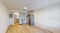 Located at 4455 W New Haven Ave in Melbourne, Florida, this efficiently designed studio unit offers a well-planned single-floor layout with two bathrooms. The open living and kitchen area is finished with light wood-tone flooring that lends warmth and visual continuity throughout the space. The kitchen is thoughtfully appointed with gray flat-front cabinetry extending to the ceiling for maximum storage, granite countertops, a classic white subway tile backsplash, and stainless steel appliances including a full-size refrigerator, dishwasher, and built-in microwave. A window with blinds allows natural light to fill the main living area, which also features a wall-mounted HVAC unit. A dedicated nook with granite countertop and wire shelving above provides additional storage and workspace. The two bathrooms are cleanly finished, with one featuring a full tub/shower combination with built-in tile shelving, a toilet, and light tile flooring. The overall aesthetic is clean and contemporary, with white walls and recessed lighting reinforcing a bright, neutral ambiance suited for efficient, modern living.
