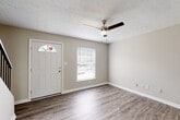 This two-story home offers a clean, functional layout designed with practicality in mind. The entry level welcomes you with durable hardwood-style flooring that flows through the main living areas, complemented by neutral warm-toned walls and crisp white trim throughout. A ceiling fan with a built-in light fixture enhances the living room, which benefits from natural light provided by a front-facing window. The staircase, featuring dark wood steps and a black metal railing, connects seamlessly to the upper level.

The galley-style kitchen is efficiently designed with ample white cabinetry, dark countertops, a double-basin sink, and stainless steel appliances including a gas range and refrigerator. Hardwood-style flooring continues here, adding cohesion to the space.

The bedrooms are finished with plush neutral carpeting and feature generous closet space, including double-door closets in multiple rooms. Natural light filters in through blinds-fitted windows, offering views of the surrounding greenery. A full bathroom serves the home with a combined tub and shower, a single vanity with a white cabinet, and matching fixtures throughout.

A textured ceiling treatment is present in select areas of the home, adding subtle visual interest to the otherwise clean and understated interior design.