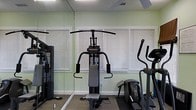 Located at 4545 Cary Glen Blvd in Cary, North Carolina, this fitness center offers a dedicated single-floor space designed to support a well-rounded workout routine. The room is appointed with light green walls that create a fresh, energizing atmosphere, complemented by natural light streaming in through multiple windows fitted with horizontal blinds. A full-length mirror spans one wall, visually expanding the space and providing a practical reference point for exercise form. The facility is equipped with a multi-function cable weight machine, ideal for a wide range of strength training exercises, as well as an elliptical trainer for low-impact cardiovascular workouts. Additional cardio and strength equipment is visible throughout the room, offering users a comprehensive set of training options. The flooring features durable, cushioned carpeting suited for gym use, and ceiling ventilation ensures comfortable air circulation during workouts. The overall ambiance is clean, functional, and focused, making this fitness center a practical and accessible amenity for residents or members seeking a convenient place to exercise.