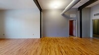 Located at 21 W North St in Akron, Ohio, this 2-bedroom, 2-bathroom unit showcases a distinctive industrial-loft aesthetic throughout its single-floor layout. The open-concept living and dining area is anchored by warm hardwood floors, exposed steel beams, and oversized industrial ductwork running overhead, lending an urban warehouse character to the space. Large multi-pane windows at the far end of the living area invite generous natural light, enhancing the bright and airy feel of the main living zone.

The kitchen is a functional centerpiece, featuring a large granite-topped island with an undermount sink and a flexible faucet, dark espresso cabinetry, and a full suite of stainless steel appliances including a gas range, built-in microwave, and refrigerator. Pendant lighting above the island adds to the modern-industrial ambiance.

Both bedrooms are carpeted for comfort and include closets with sleek frosted-glass sliding doors framed in black. The hallway connecting the bedrooms continues the carpet flooring and features rich wood-toned doors. The two bathrooms are finished with tile flooring — one includes a tub-shower combination, while the other offers a standalone glass-enclosed shower with a dark wood vanity. A dedicated utility room and multiple closets provide ample storage throughout.