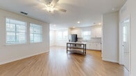 This single-floor unit is designed with a clean, contemporary aesthetic, showcasing light-toned luxury vinyl plank flooring throughout the main living areas and soft carpeting in the bedrooms. The open-concept layout connects the living area to the kitchen, creating a spacious, airy feel enhanced by abundant natural light flowing through multiple windows fitted with horizontal blinds. Ceiling fans are present in the living area and bedrooms, contributing to a comfortable environment.

The kitchen is well-appointed with white shaker-style cabinetry extending to the ceiling, light quartz countertops, a subway tile backsplash, and stainless steel appliances including a range, microwave, dishwasher, and refrigerator. A stainless steel undermount sink sits beneath a window, adding natural light to the workspace.

The bedrooms are generously sized, each featuring plush carpet, neutral walls, and windows with outdoor views. The bathroom includes a walk-in glass-enclosed shower with white tile surround, while a secondary bathroom offers a tub-shower combination. A dedicated laundry area with in-unit washer and dryer connections adds further convenience. The hallway provides seamless access to all rooms, maintaining a practical and cohesive flow throughout the space.
