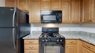 Located at 27 Independence Dr in Methuen, Massachusetts, this single-floor unit offers a practical and comfortable layout with consistent light wood-style flooring throughout. The kitchen is thoughtfully equipped with warm honey-toned cabinetry, granite countertops, and black appliances including a gas range with over-the-range microwave, a refrigerator, and a dishwasher — providing ample storage and functionality for everyday cooking. An open sightline connects the kitchen to the adjacent living area, creating a cohesive and easy-to-navigate floor plan. The living room is a generously sized, light-filled space featuring a sliding glass door that opens to a private balcony overlooking lush greenery, along with a wall-mounted air conditioning unit and baseboard heating. The bedrooms are well-proportioned, each featuring windows that bring in natural light, baseboard heating, and air conditioning units. One bedroom includes a sliding-door closet with built-in shelving. The bathroom features a full soaking tub and shower combination with clean white tile surround and modern chrome fixtures. Throughout the unit, neutral gray walls complement the light flooring, creating a bright and cohesive aesthetic.