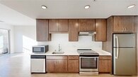 This single-floor unit offers a clean, modern design with a functional layout spread across several distinct areas. The kitchen is a standout feature, outfitted with rich medium-toned wood cabinetry extending to the ceiling for generous storage, light-colored countertops, and a full suite of stainless steel appliances including an electric range, refrigerator, dishwasher, and microwave. Recessed lighting illuminates the space, and a single-basin sink with a contemporary faucet completes the setup.

The living area is bright and open, featuring light hardwood-style flooring and white walls that enhance the sense of space. A sliding glass door leads to an outdoor balcony, allowing natural light to fill the room. Adjacent areas share the same light flooring and neutral palette, providing a cohesive flow throughout.

The bedrooms feature soft carpeting and large windows that bring in natural light and exterior views. Each room offers a clean, versatile canvas with ample wall space. The bathroom includes a vanity with wood cabinetry and a well-lit mirror. A dedicated laundry room with an in-unit washer, wood-style flooring, and built-in shelving adds everyday convenience to this well-appointed space.