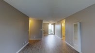 This single-floor residence offers a clean, functional layout designed to maximize comfort and usability. The main living area is open and airy, finished with warm wood-look hard-surface flooring that runs throughout, providing a cohesive and low-maintenance aesthetic. Neutral gray walls complement the white baseboards and trim, creating a modern yet understated palette throughout the space. A textured ceiling adds subtle depth to the interior.

Natural light flows into the living area through a set of sliding glass doors, which offer a view of the outdoors and provide easy access to an exterior space. A ceiling fan positioned in this area promotes air circulation and adds a casual, practical touch to the room.

Adjacent to the main living space, a hallway connects to additional rooms, including what appears to be a well-lit secondary space — possibly a bedroom or utility area — finished with matching flooring and warm lighting. The layout is straightforward and efficiently organized, with clear sightlines from the entry through to the back of the residence.

Overall, the space presents a bright, well-maintained interior with consistent finishes, practical features, and a welcoming ambiance suited for everyday living.