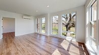 This contemporary 2-bedroom, 2-bathroom unit at 100 Hamilton St in Bound Brook, NJ offers a thoughtfully designed open-concept layout with modern finishes throughout. The living area is expansive and sun-drenched, featuring large floor-to-ceiling windows that frame outdoor views of mature trees and green surroundings, complemented by light-toned hardwood-style flooring and clean white walls. The kitchen is a standout centerpiece, showcasing a sizeable island with a wood-paneled base and white countertop, white upper cabinetry, stainless steel appliances including a refrigerator, range, and microwave, and a window that fills the cooking area with natural light. Each bedroom is generously proportioned, offering wide windows with outdoor views, individual wall-mounted mini-split HVAC units, and the same warm hardwood-style flooring. The primary bathroom features a sleek glass-enclosed walk-in shower, wood-toned vanity cabinetry, and light tile flooring, while the second bathroom includes a tub-shower combo with white subway tile surround. The unit also includes a dedicated closet and a hallway with a utility panel. Black hardware accents throughout add a refined, contemporary touch to the overall aesthetic.
