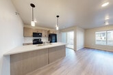 Located at 3201 N. Martindale Rd in Sioux Falls, SD, this 1-bedroom, 2-bathroom unit offers a thoughtfully designed single-level layout. The open-concept living and kitchen area serves as the heart of the home, featuring light vinyl plank flooring, neutral tones, and large windows that invite natural light throughout. The kitchen is equipped with warm taupe cabinetry, a spacious peninsula with a white countertop and built-in sink, black appliances including a refrigerator, electric range, and over-the-range microwave, all illuminated by stylish pendant lighting. A sliding glass door connects the living area to an outdoor patio. The bedroom is carpeted for comfort, includes a ceiling fan, and benefits from a window with natural light. The two bathrooms are finished with light tile flooring, a tub-shower combination, and taupe vanity cabinetry with a white countertop. A dedicated laundry area with washer and dryer hookups adds everyday convenience. The unit's clean, modern aesthetic, efficient use of space, and practical finishes make it a functional and comfortable residence.