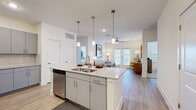 This single-story, 2-bedroom, 2-bathroom residence offers a thoughtfully designed open-concept layout with modern finishes throughout. The kitchen serves as a central hub, anchored by a large island with granite countertops, a double-basin sink, and seating for multiple bar stools. Three pendant lights hang above the island, complementing the stainless steel appliances, gray cabinetry, and herringbone tile backsplash. Light wood-look flooring extends seamlessly from the kitchen into the living room, which features a ceiling fan, French doors providing generous natural light, and direct access to an outdoor area.

The primary bedroom is a comfortable retreat with plush carpet, a ceiling fan, large windows, and an en-suite bathroom featuring a dual-sink granite vanity, gray cabinetry, and a bathtub with shower. A spacious walk-in closet with built-in shelving and hanging rods adds practical storage. The second bedroom is equally well-lit with carpet flooring and a dedicated closet. The second bathroom mirrors the primary's refined finishes. Three total closets ensure ample storage throughout this bright, efficiently arranged residence.