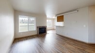 Located in Lakewood, WA, this one-bedroom, one-bathroom residence offers a well-organized single-level layout with a thoughtful mix of comfort and functionality. Wood-style flooring runs throughout the entire unit, lending warmth and visual continuity to every room. The combined living and dining area is generously proportioned, anchored by a tile-surround fireplace and framed by large windows that fill the space with natural light and provide pleasant outdoor views. A pass-through counter connects the living area to the galley-style kitchen, which is equipped with warm oak cabinetry, light countertops, white appliances including a refrigerator, range, and dishwasher, and a stainless steel sink. The bedroom is a comfortable size, featuring a sliding double-door closet and recessed lighting, with additional storage accessible nearby. The bathroom includes a full soaking tub and shower combination with chrome fixtures and clean white finishes. A dedicated laundry area adds everyday convenience, while the private balcony provides an outdoor retreat. A hallway with a coat closet connects the rooms and enhances the overall flow of the layout, making this a practical and inviting living space.