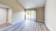 Located at 2405 Walnut Ave in Carmichael, California, this 2-bedroom, 1-bathroom residence offers a well-organized single-floor layout that makes efficient use of its space. The interior is finished with a clean, neutral color palette of warm beige tones and crisp white trim throughout.

The living room is a standout feature, boasting vaulted ceilings that lend a sense of openness, light wood-look laminate flooring, and sliding glass doors that connect directly to a private balcony with outdoor views of surrounding greenery. A thermostat and ceiling vent indicate a central HVAC system for year-round comfort.

The kitchen is functionally designed in a galley style, featuring white cabinetry, light countertops, a stainless steel sink, and white appliances including a refrigerator and electric range. A pass-through counter connects the kitchen to the dining area, enhancing the flow between spaces.

Both bedrooms are carpeted with soft, neutral-toned carpet and feature textured ceilings and natural light from windows with blinds. The primary bedroom includes a spacious sliding-door closet. Additional closets throughout provide generous storage.

The bathroom is well-appointed with a full tub-shower combination, a white vanity with a large mirror, and light wood-look flooring. A dedicated entrance, hallway, and three closets round out this thoughtfully arranged home.